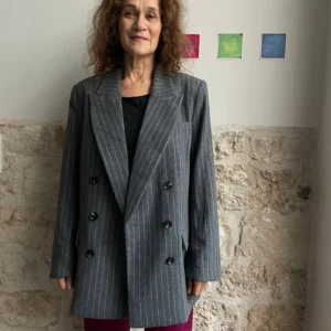 Une femme portant une veste tailleur H&M avec un tee-shirt noir et un pantalon prune, debout dans une pièce